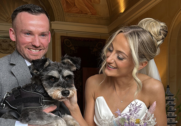 Bride and groom smile while groom holds dog